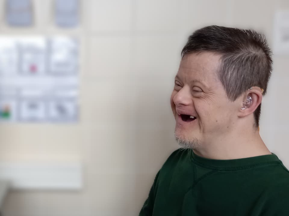 Lachende bewoner tijdens een videogesprek, met een hoortoestel achter zijn oor.