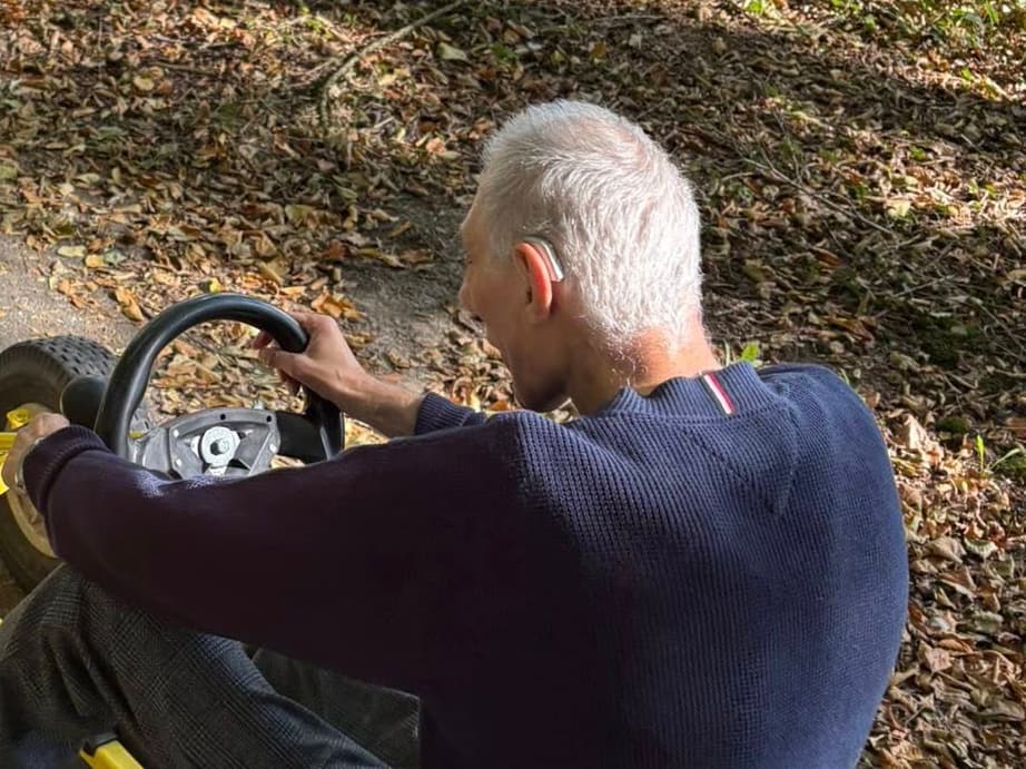 Bewoner rijdt met een go-cart door het bos en draagt hoortoestellen.