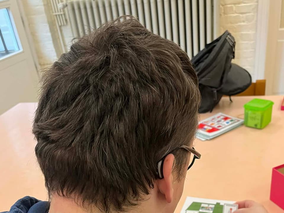 Bewoner werkt aan tafel met pictogrammen en draagt een hoortoestel achter het oor.