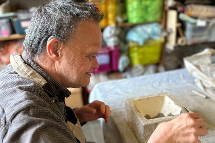 Bewoner met hoortoestel werkt aan een keramiekstuk in het atelier.